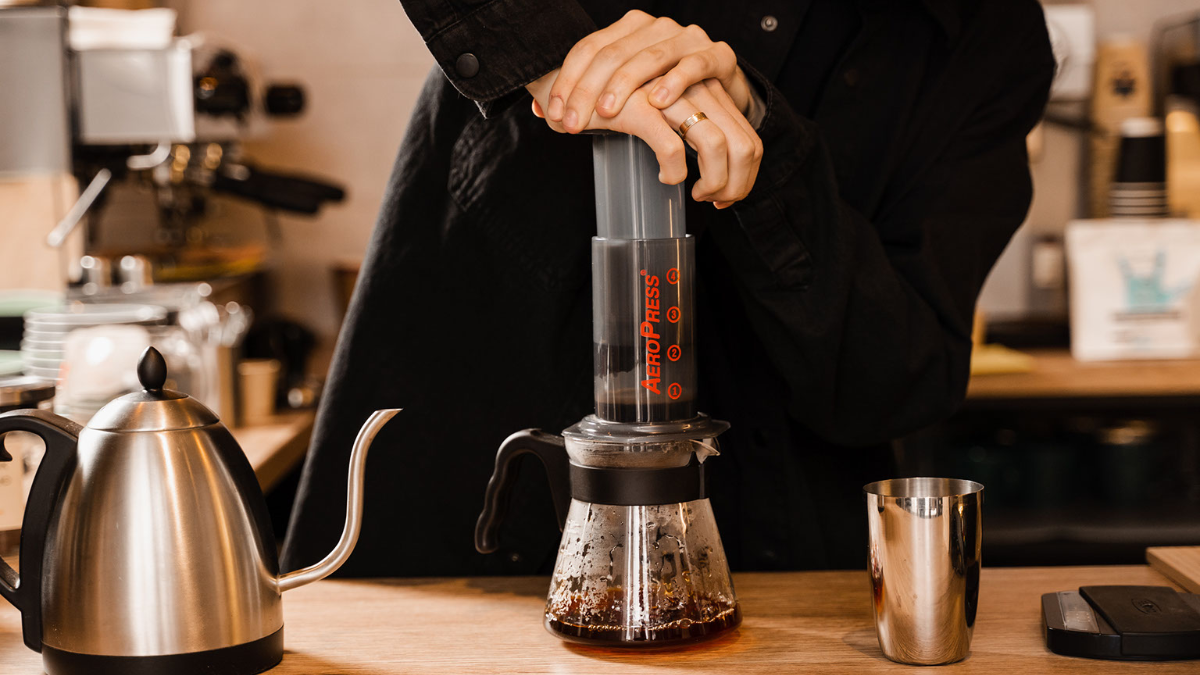 A man using an AeroPress, pushing down with both hands as fresh coffee pours into a glass jar.