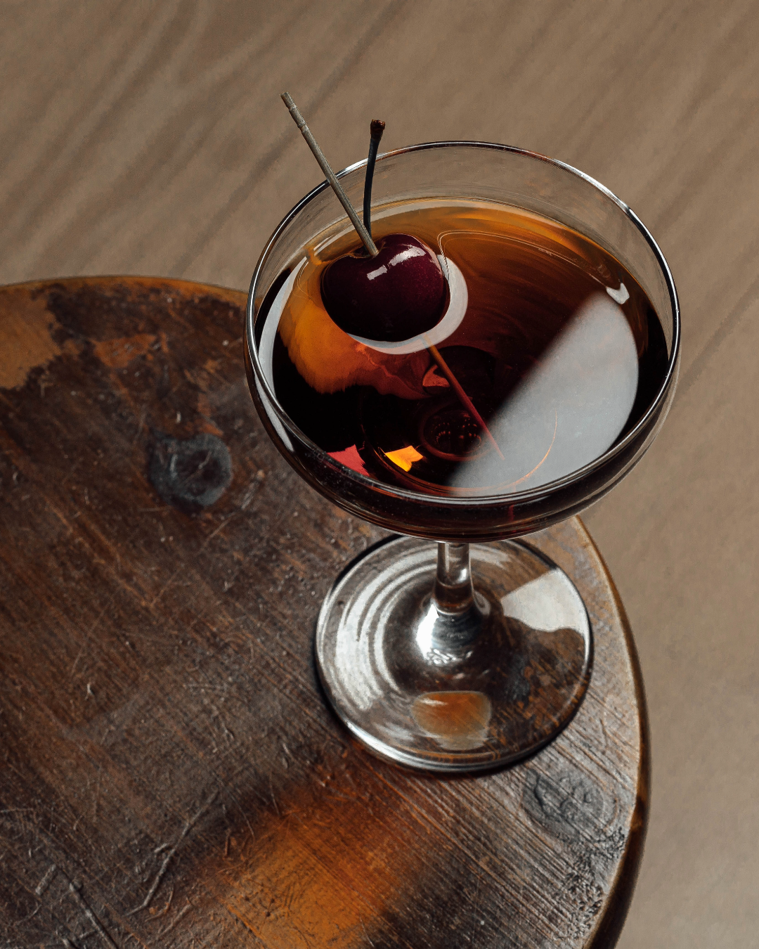 Black Manhattan Cocktail garnished with a cherry on a dark wooden surface
