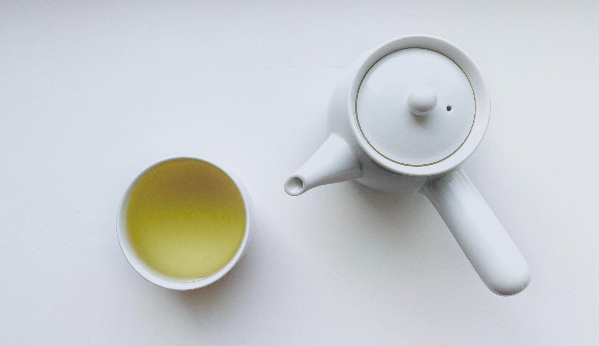 top view of a white teapot next to a white tea cup full of white tea.